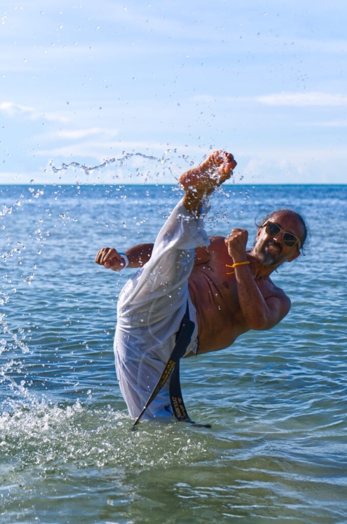 Trainer bei einem Sprungkick im Meer, Wasser spritzt