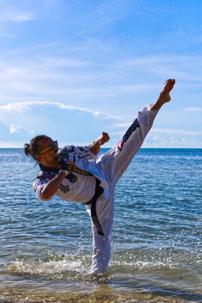 Taekwondoin im Dobok bei einem hohen Seitwärtskick im Meer